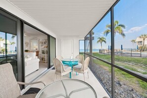 A modern room with a glass door leading to a balcony, a round table with chairs, and a view of the beach.