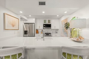Una cucina moderna con mobili bianchi, elettrodomestici in acciaio inossidabile e un'isola centrale con sedute.