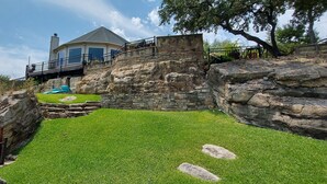 Une maison avec un mur de soutènement en pierre, une piscine et une cour gazonnée.