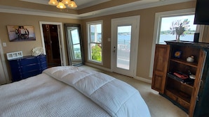 Une chambre avec un grand lit, une commode, un téléviseur et une vue sur un balcon doté d’une balustrade.