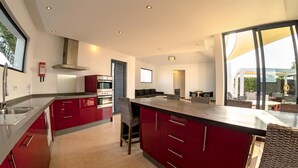 A modern kitchen with red cabinetry, stainless steel appliances, and a large island. - Casa Yuna with heated pool in El Roque (El Roque)