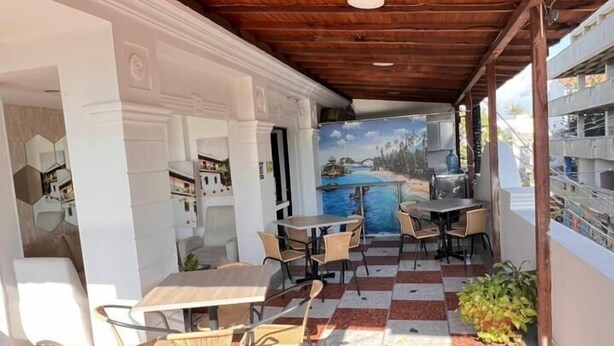 An outdoor patio with a checkered floor, wooden ceiling beams, and a mural of a beach scene. - Hotel Tayromar (Santa Marta)
