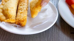 A hand picking up a fried item from a plate, with another plate containing sliced bread and a slice of watermelon in the background. - Hotel Tayromar (Santa Marta)
