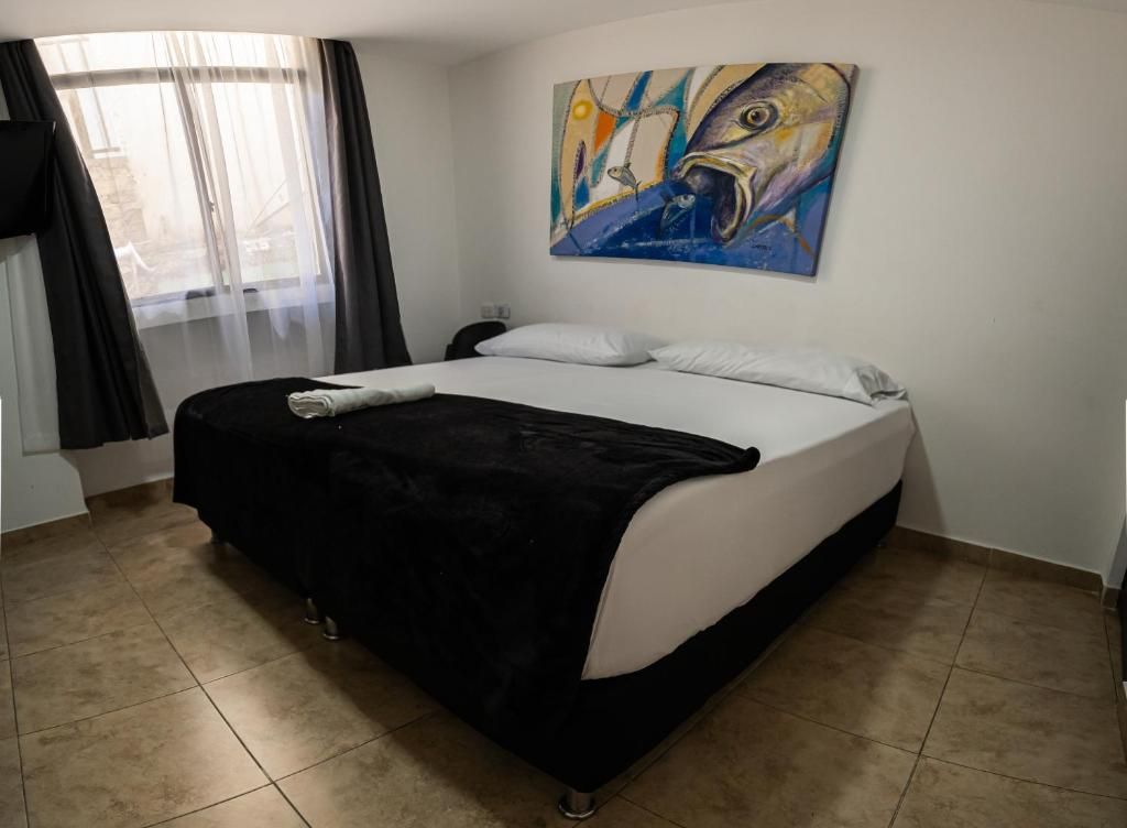 A hotel room with a bed, a painting on the wall, and a window with curtains.