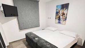 A room with a bed, a flat-screen TV mounted on the wall, a window with a blind, and a painting on the wall. - Hotel Tayromar (Santa Marta)