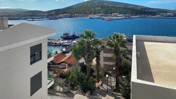 A coastal view with a marina, boats, and a hill with wind turbines. - Azize Palas Apart (Cesme)