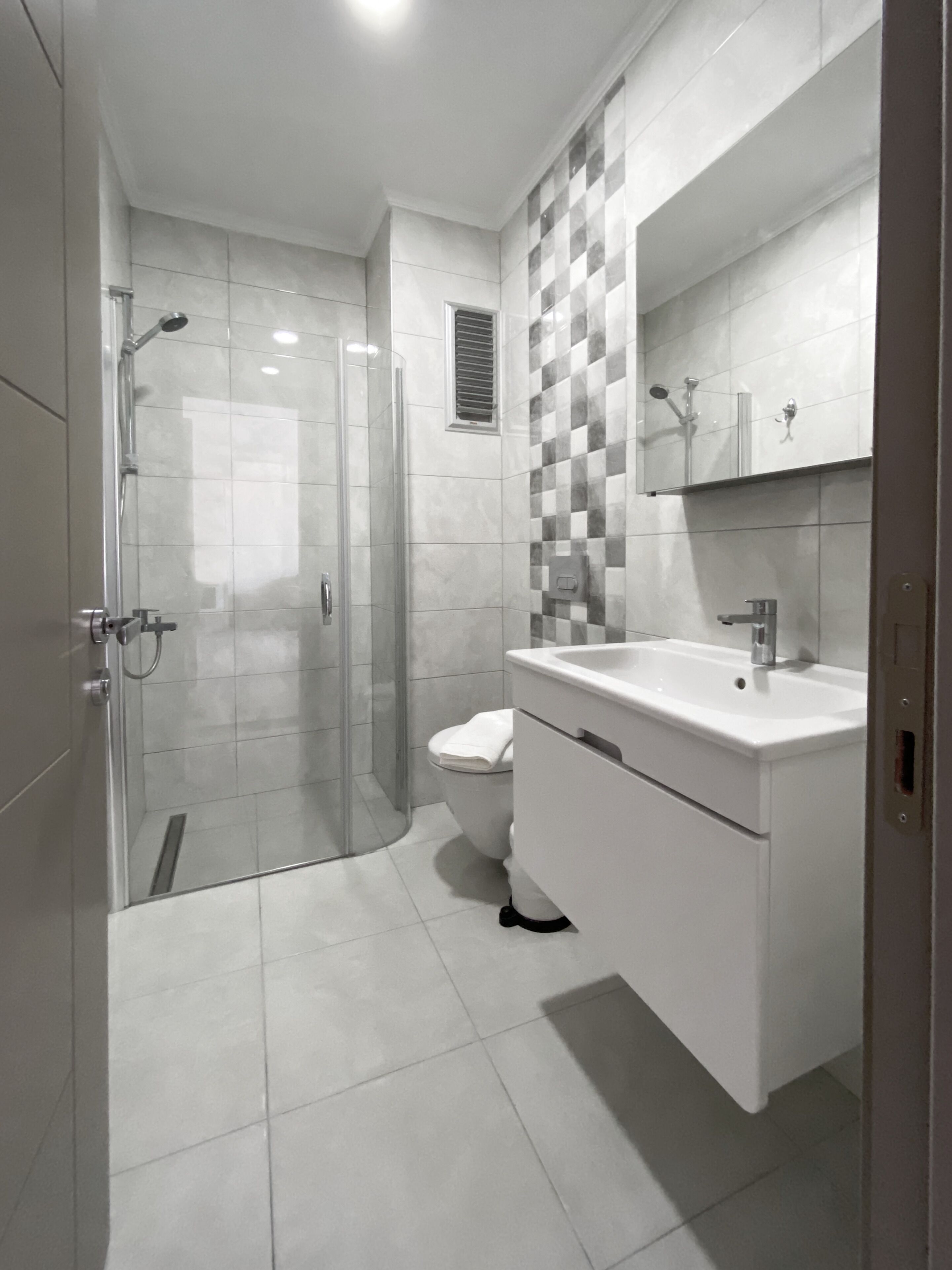 A modern bathroom with a glass shower enclosure, a toilet, and a vanity with a sink and mirror.