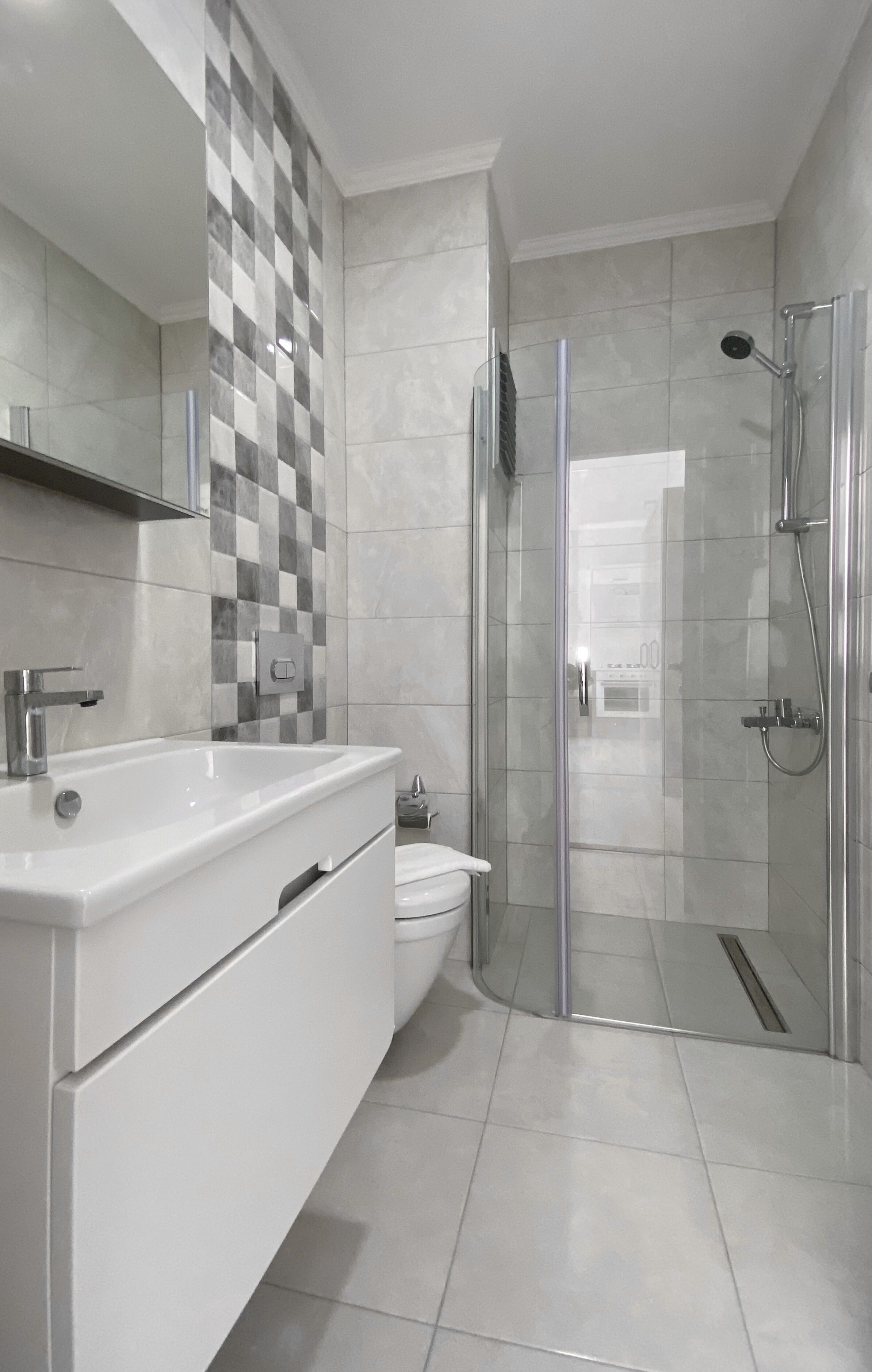 A modern bathroom with a white vanity, a glass shower enclosure, and a checkered tile backsplash.