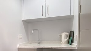 A compact kitchen with white cabinets, a stainless steel faucet, a kettle, and a small countertop. - Azize Palas Apart (Cesme)