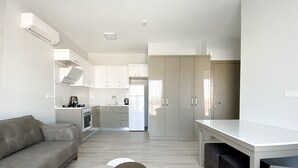 A modern kitchen with white cabinets, a built-in oven, and a refrigerator. There is a dining area with a white table and two chairs. - Azize Palas Apart (Cesme)