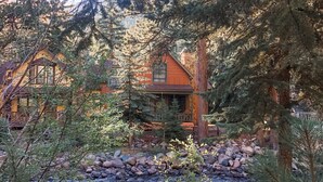 A cabin with a wooden exterior, surrounded by dense forest and a flowing stream. - Riverfront Mountain Cottage Retreat (Estes Park)