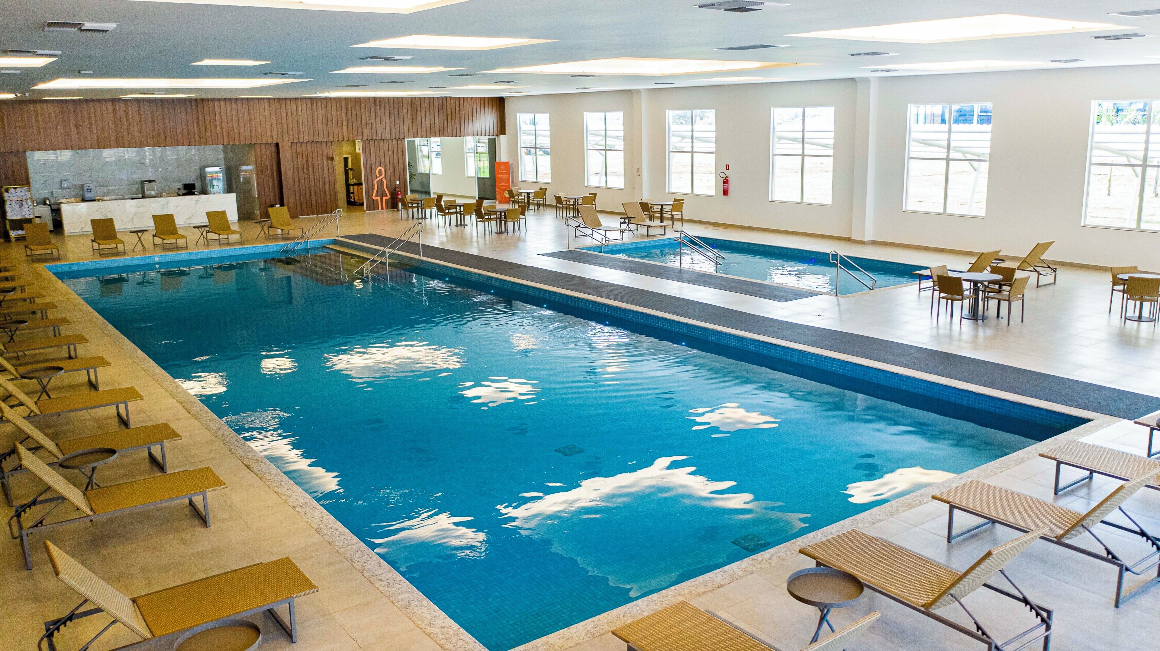 Uma grande piscina coberta com várias pistas de natação, espreguiçadeiras e uma área de recepção.