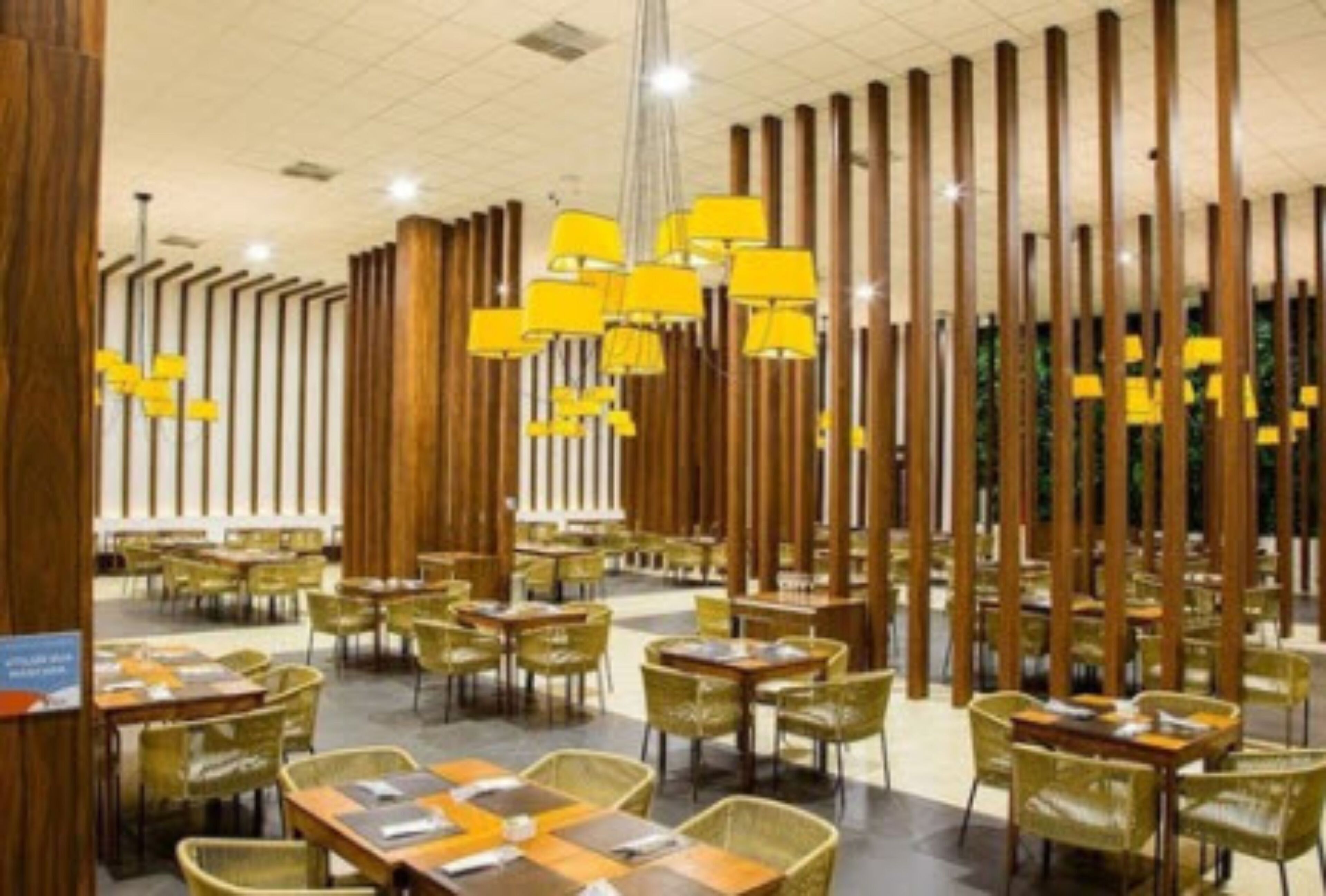 Restaurante com divisórias de madeira altas, luminárias pendentes amarelas e cadeiras verdes.