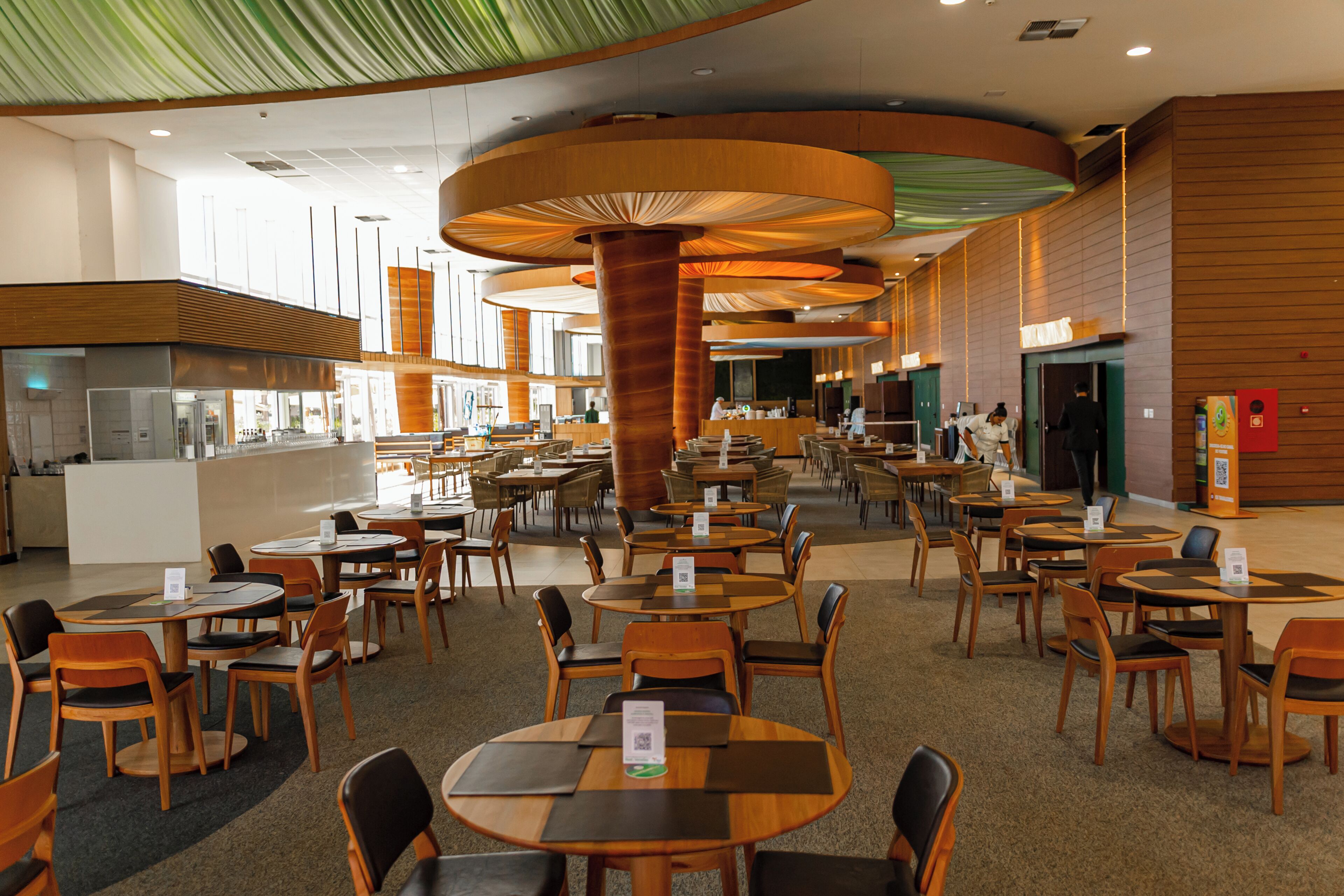 A spacious indoor dining area with multiple tables and chairs, a central column, and a counter area in the background.