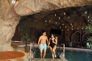 A man and woman walking towards a pool in a cave-like setting with hanging lights and a bar area in the background. - Tauá Resort & Convention Alexânia (Alexania)