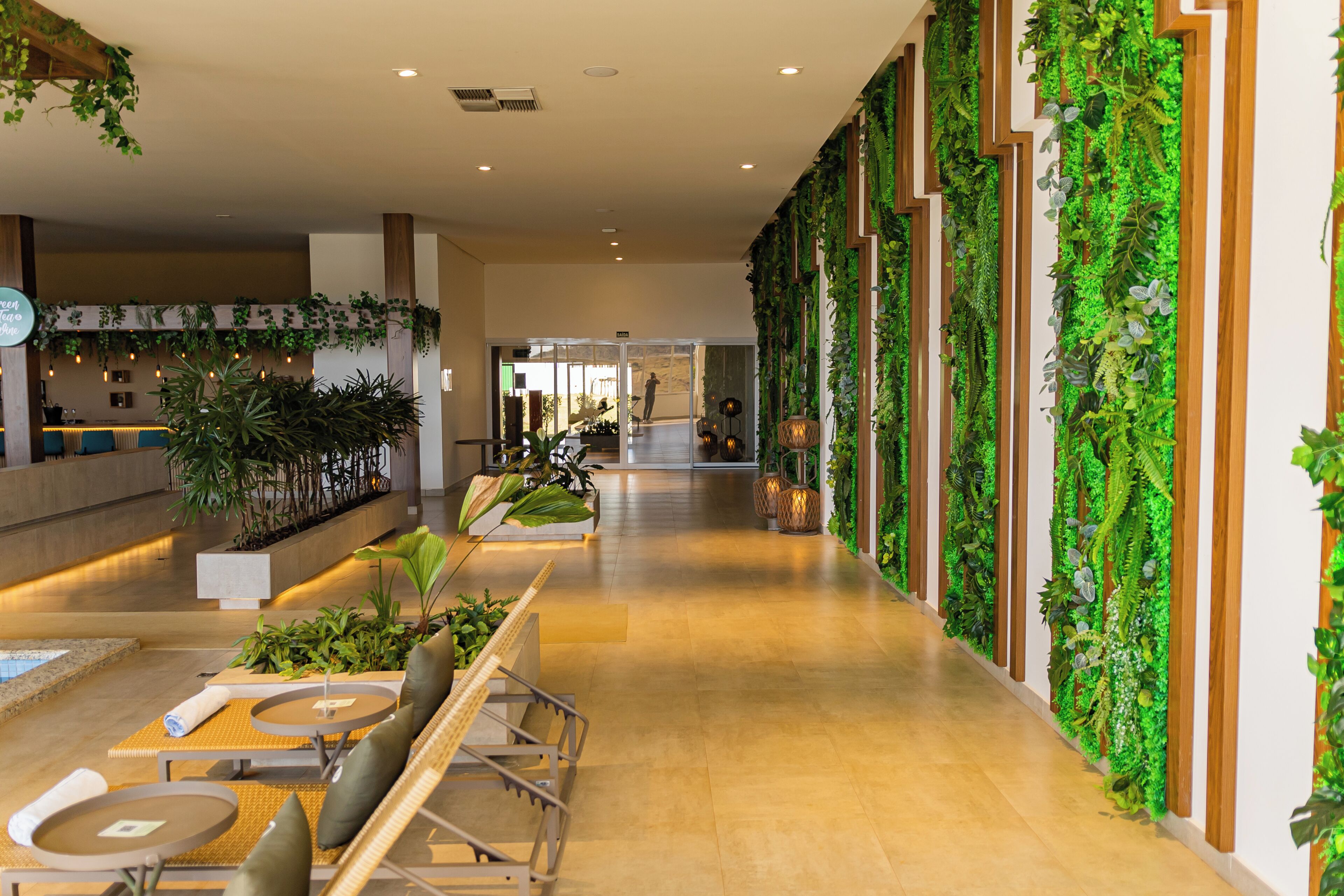 A hotel lobby with a long corridor, seating area with tables and chairs, and a wall adorned with vertical greenery.