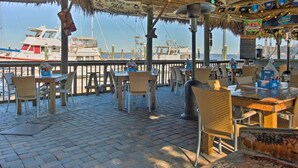 Un espacio para comer al aire libre con mesas y sillas, con vista a un puerto deportivo lleno de barcos.