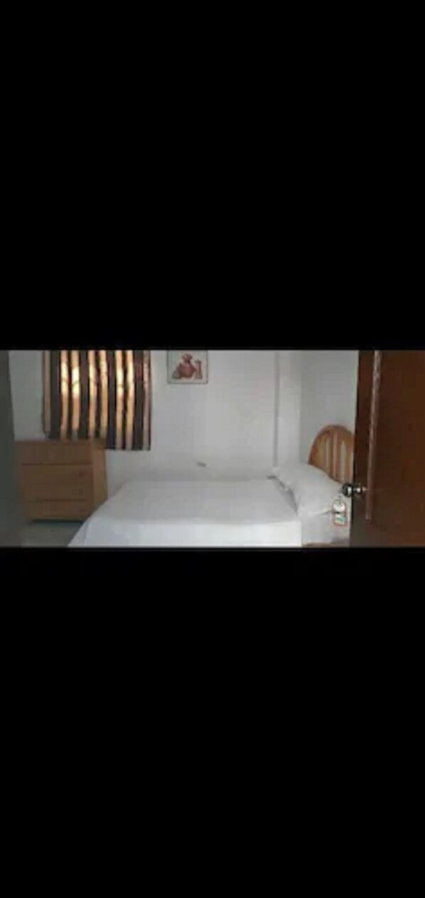 Una habitación pequeña y sencilla con una cama individual, un aparador de madera y una puerta.