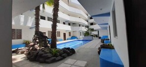 A multi-level hotel with a central swimming pool, surrounded by palm trees and stone features. - Grand Hotel Paraiso Salinas (Salinas)