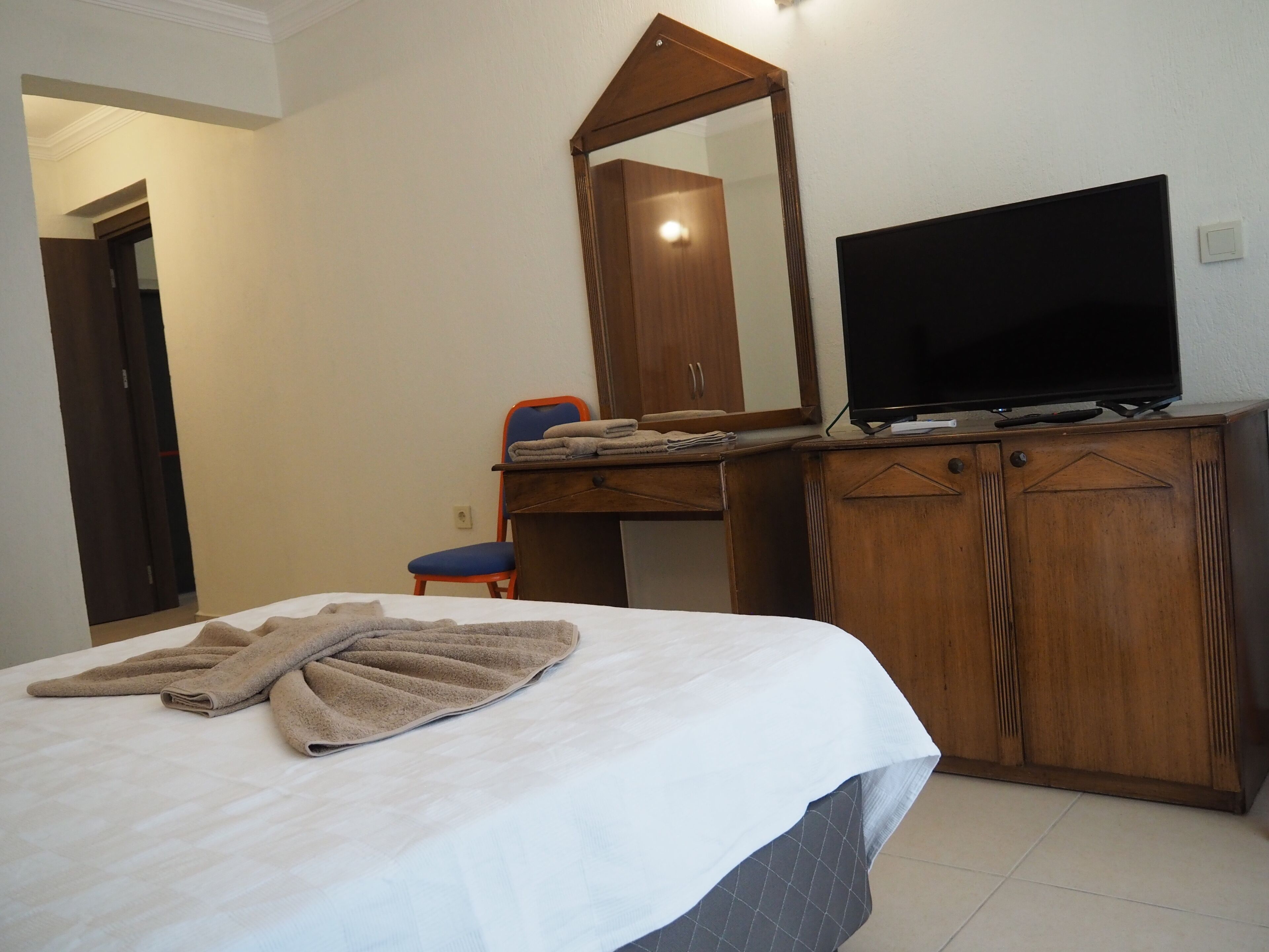A hotel room with a bed, a television on a wooden cabinet, a chair, and a mirror.