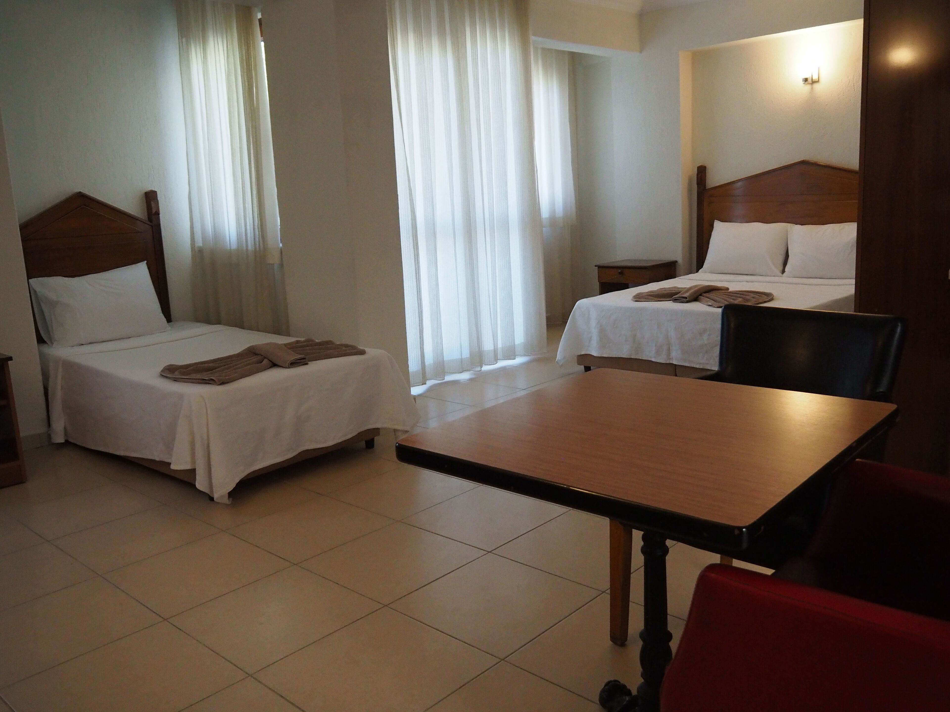 A hotel room with two single beds, a wooden table, and a red chair.