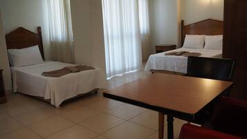 A hotel room with two single beds, a wooden table, and a red chair.