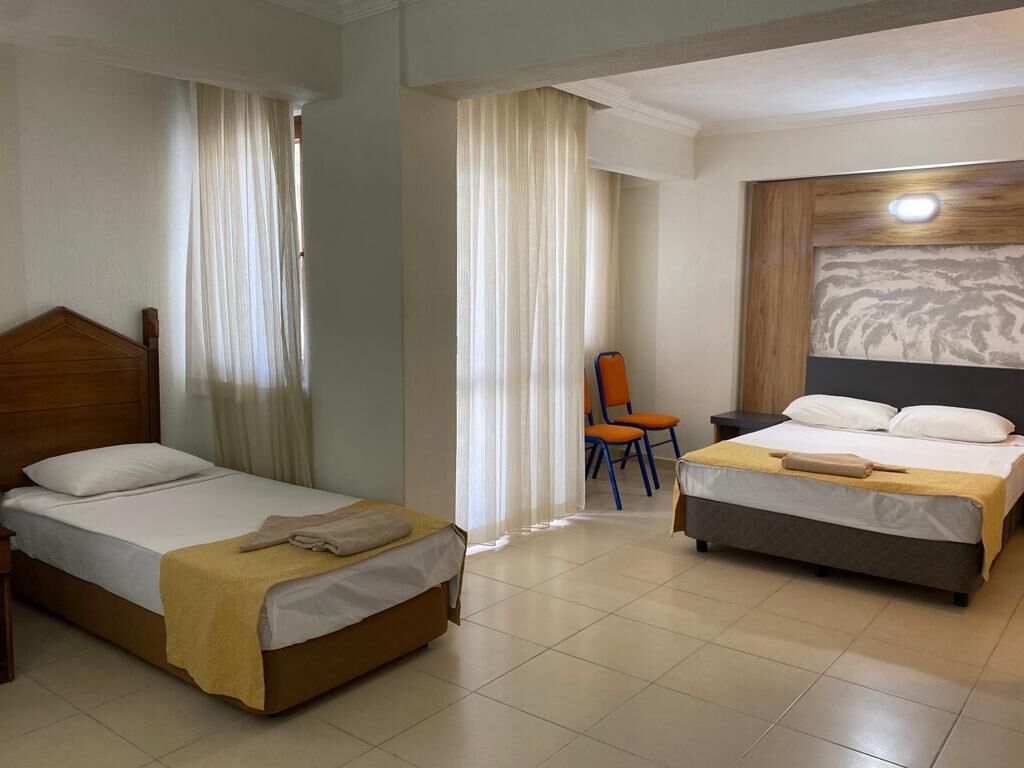A hotel room with two single beds, a wooden headboard, a small table, and a chair.
