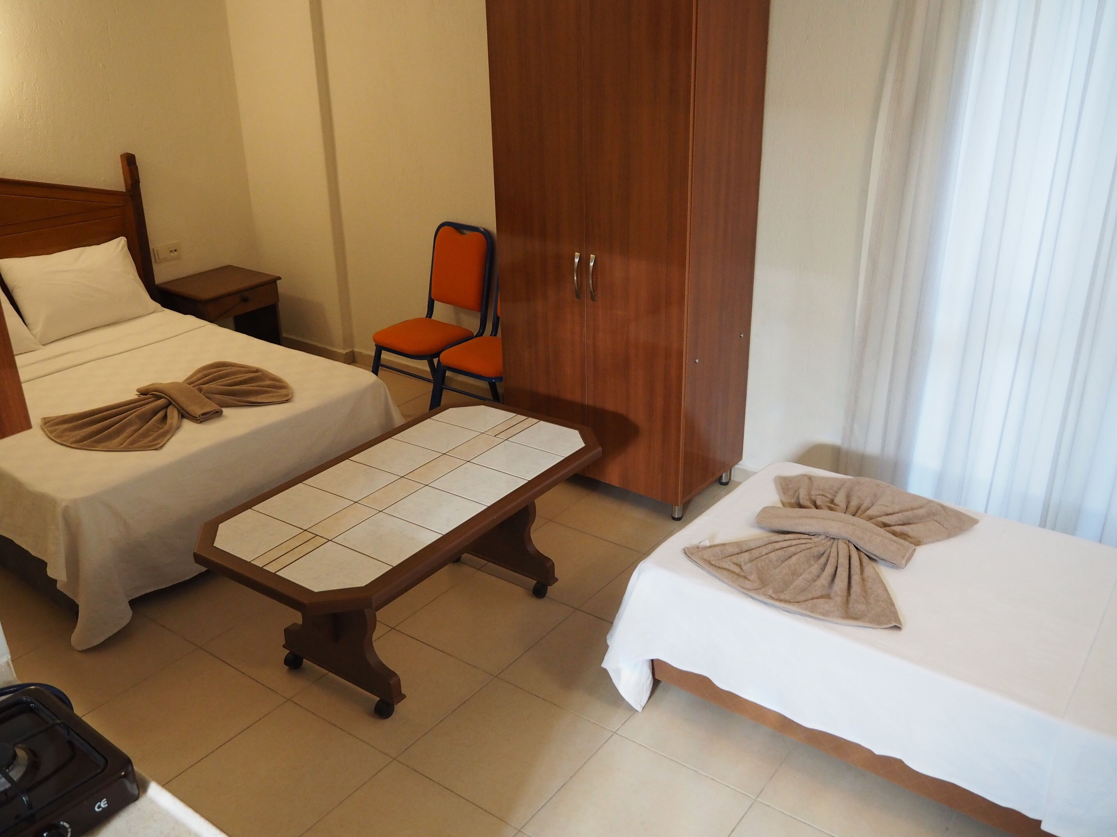 A hotel room with two beds, a wooden wardrobe, an ironing board, and an orange chair.