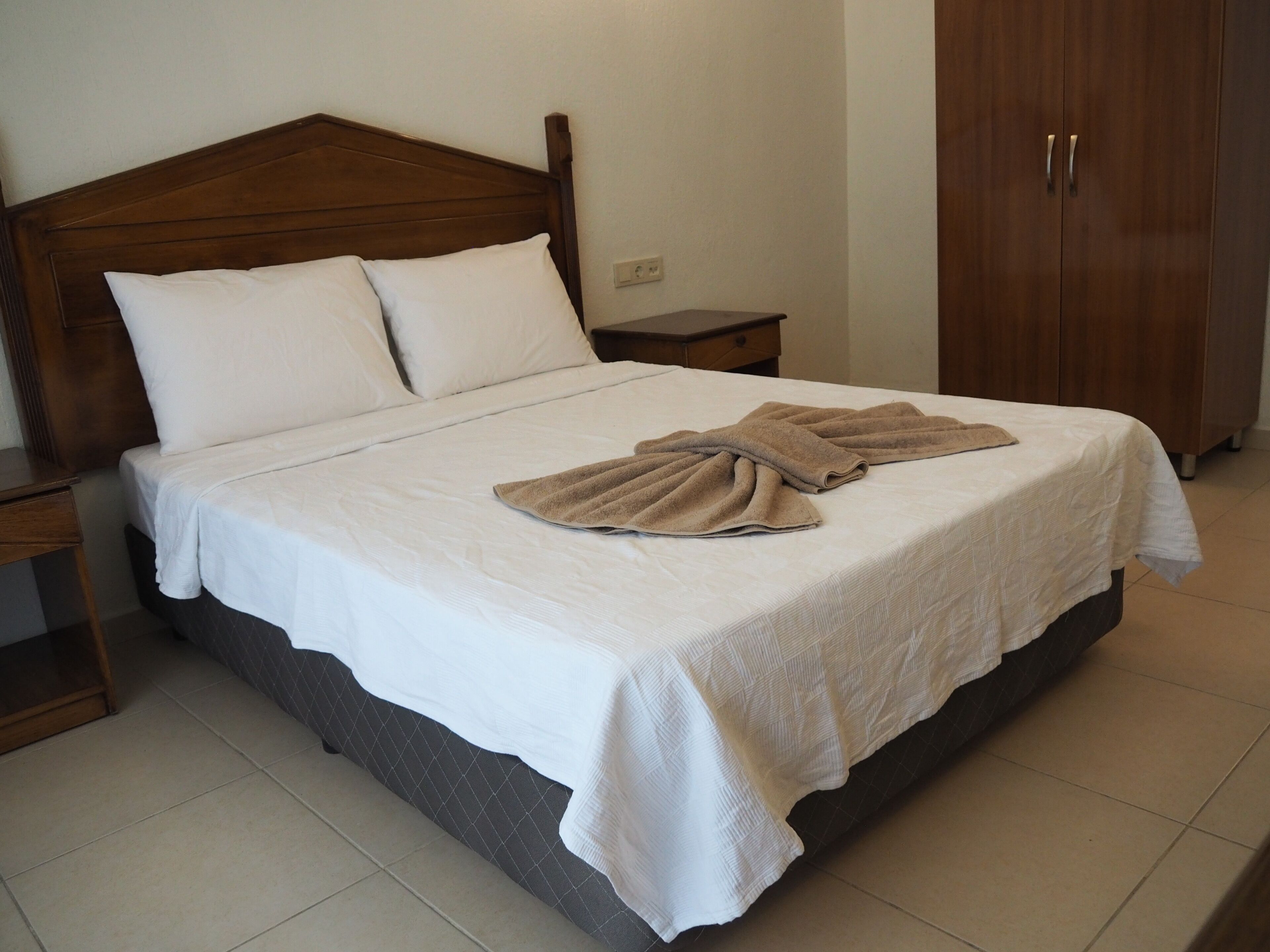 A neatly made bed with white linens and two beige towels folded on top.