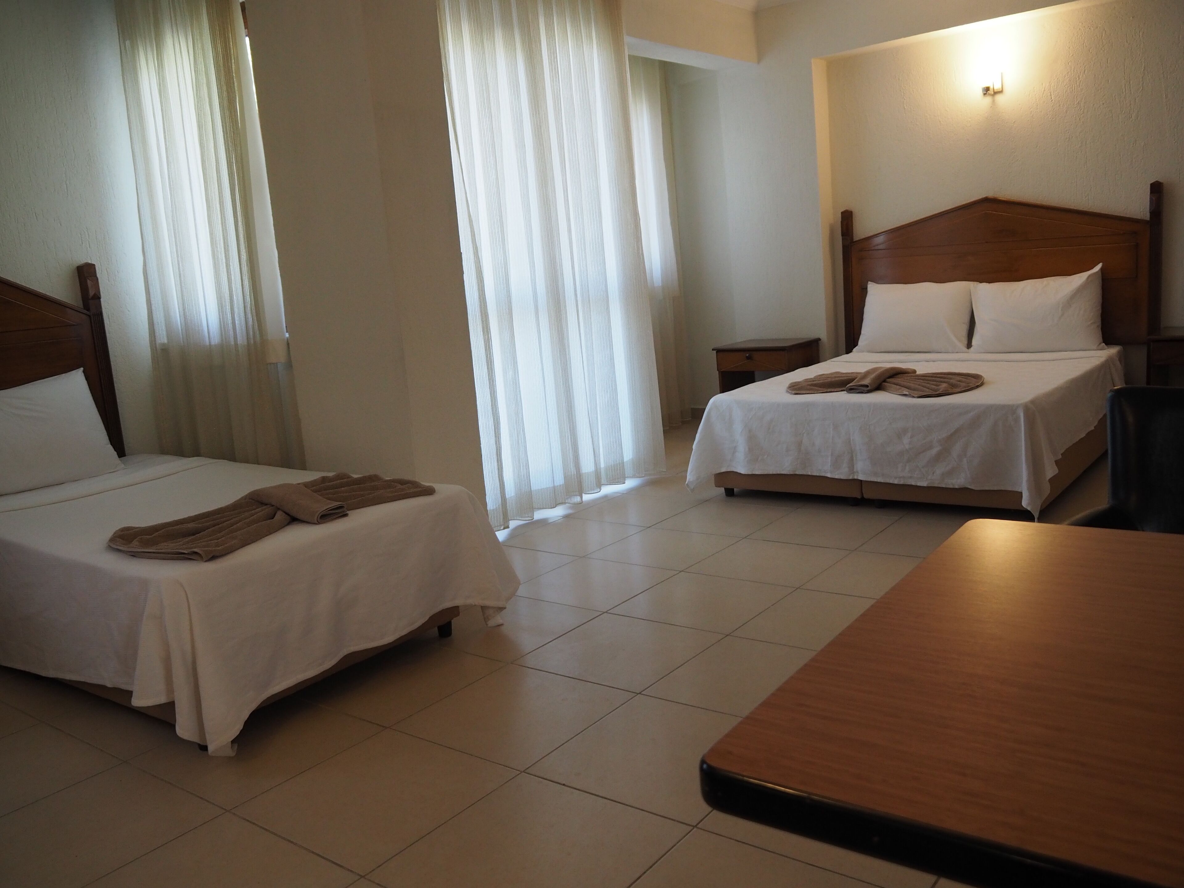 A hotel room with two beds, a wooden headboard, a nightstand, and a table.