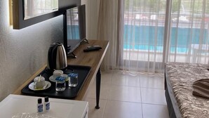Habitación de hotel con cama, escritorio con computadora, televisión y ventana con vista a una piscina.