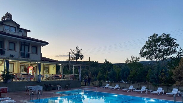 Una piscina con sillones, un restaurante con terraza y un edificio con balcón.