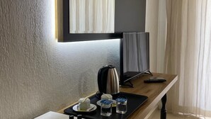 Habitación de hotel con un lavamanos blanco, un espejo, una mesa de madera con una tetera, tazas y un control remoto.