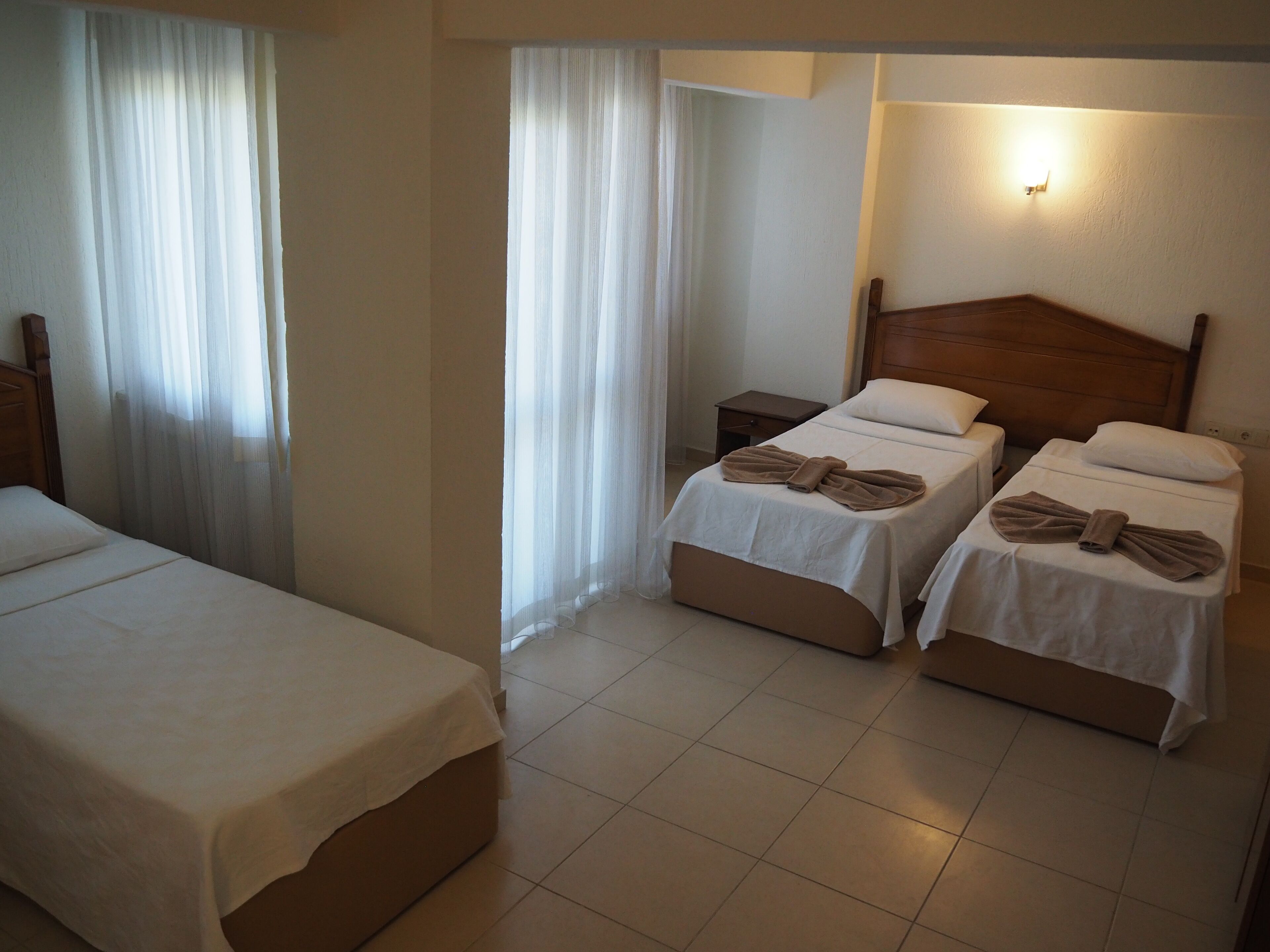 A hotel room with two single beds, a nightstand, and a wall-mounted light.