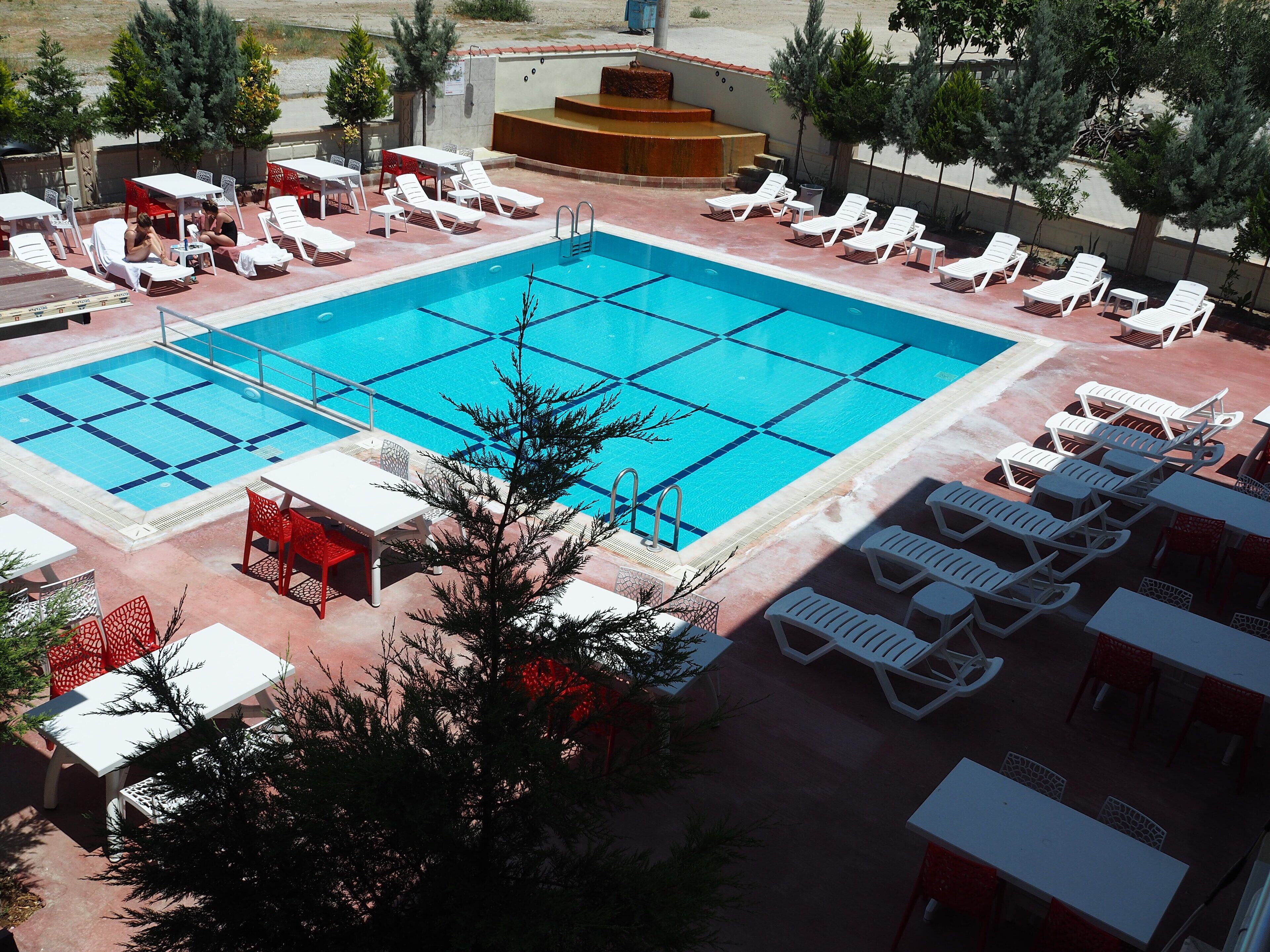 A swimming pool with white lounge chairs and red chairs, surrounded by tables and potted plants.