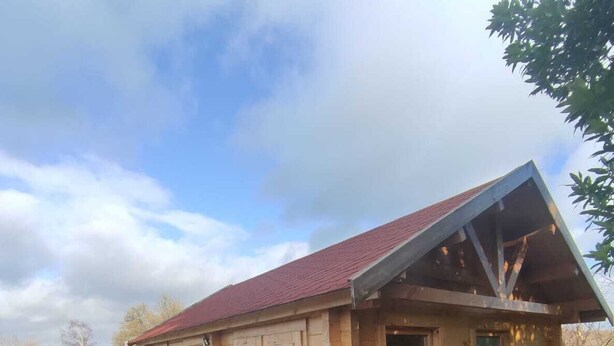 Una cabaña de madera con techo rojo, ventanas grandes y una terraza de madera.