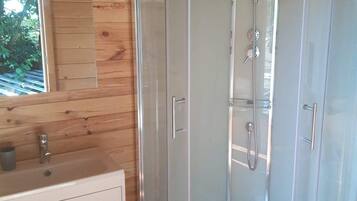 A modern bathroom with a glass-enclosed shower, wooden panel walls, a white sink, and a window with a view of greenery.