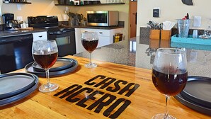 A kitchen with a wooden table displaying 'CASH ACERO' and three glasses of red wine. - Casa Acero - hot tub spa, comfortable, views, private (Alpine)