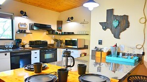 A modern kitchen with a wooden table set for four, a coffee station, and a Texas state decoration on the wall. - Casa Acero - hot tub spa, comfortable, views, private (Alpine)