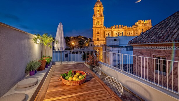 A rooftop terrace with a wooden table, potted plants, and a view of a historic building with a clock tower.