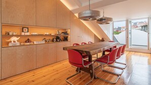 A modern kitchen with wooden cabinets, a long dining table with red chairs, and a large window offering a view of buildings. - Olá Lisboa Apartment (Lisboa)
