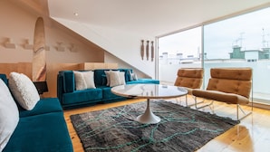 A modern living room with a teal sofa, a round coffee table, and a large window offering a view of the cityscape. - Olá Lisboa Apartment (Lisboa)