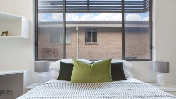 A bedroom with a large window, a bed with green and white bedding, and two bedside lamps. - Cosy and Bright Studio Next to Westmead Hospital (Westmead)