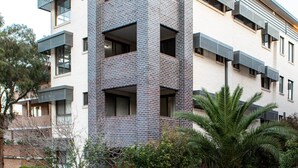 Un immeuble à plusieurs étages, doté d’une façade en briques, de balcons et d’un espace paysager agrémenté d’arbres et d’arbustes.