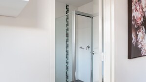 Une salle de bain moderne dotée d’une douche à parois de verre, de murs carrelés et d’une œuvre d’art florale encadrée accrochée au mur.