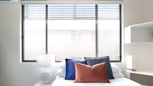 Une chambre à coucher avec un lit, des oreillers, une lampe, une fenêtre et une table de chevet.