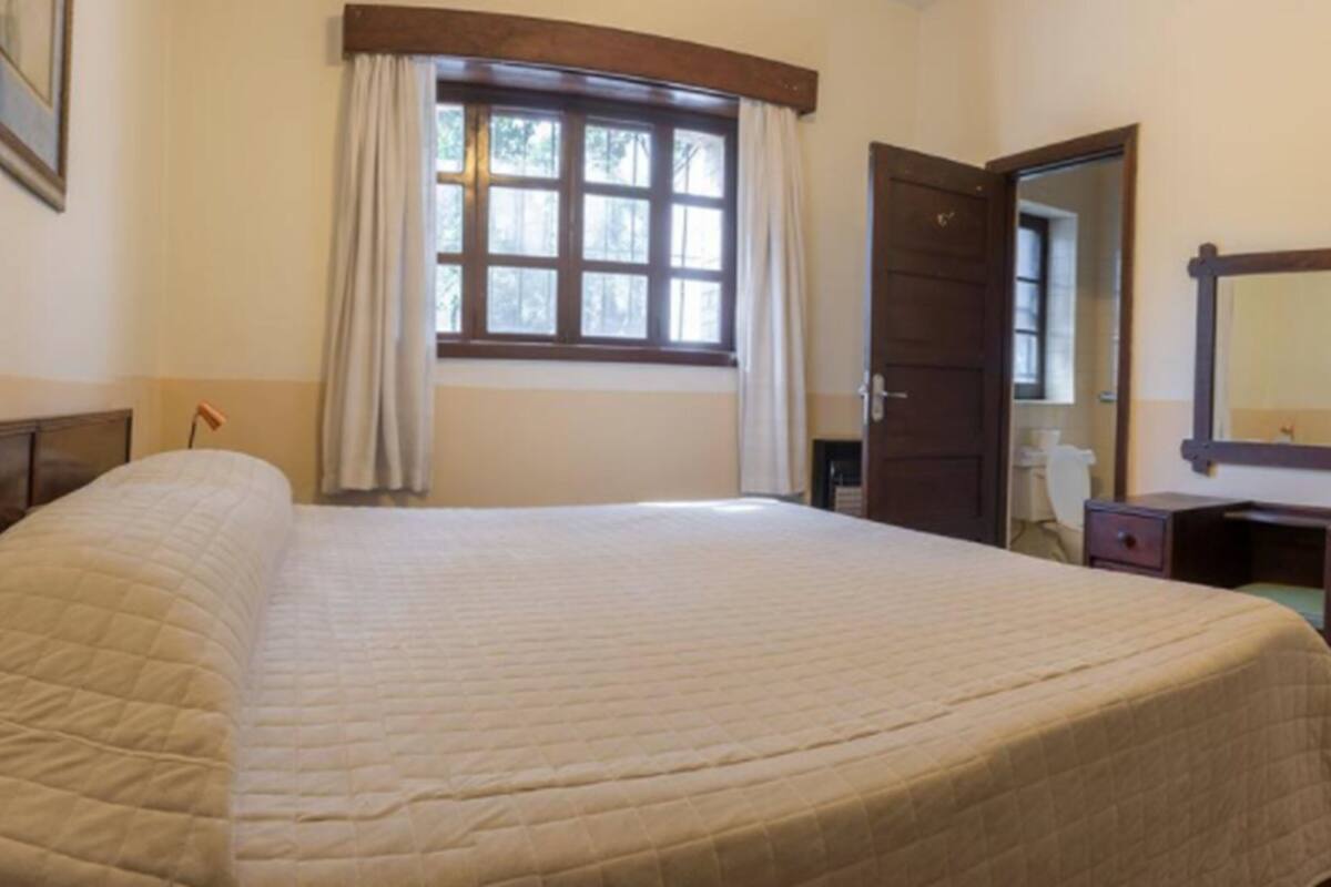 Un dormitorio con una cama grande, un aparador de madera, un espejo y una ventana con cortinas.