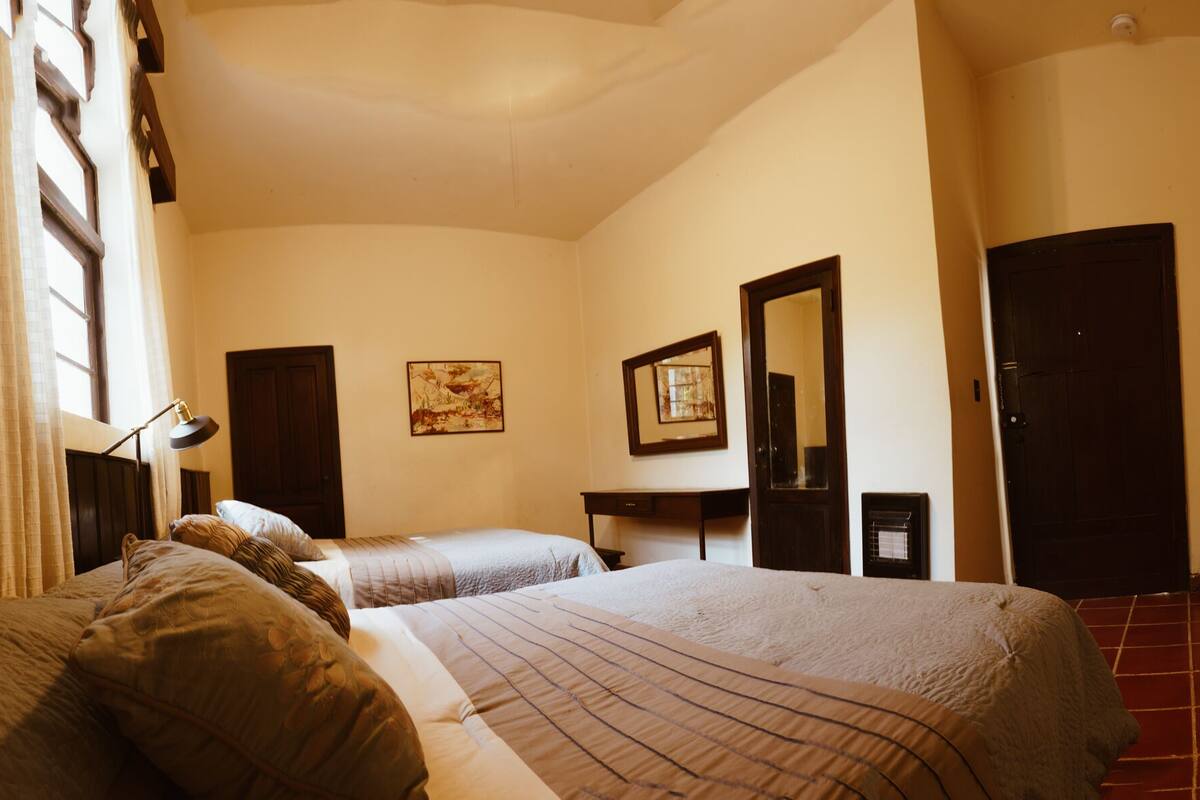 Habitación de hotel con dos camas, un escritorio, una silla, una lámpara y un espejo grande.
