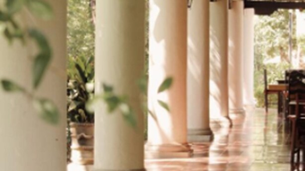 Área externa coberta com colunas e piso de azulejos, possivelmente parte de um hotel ou edifício público.