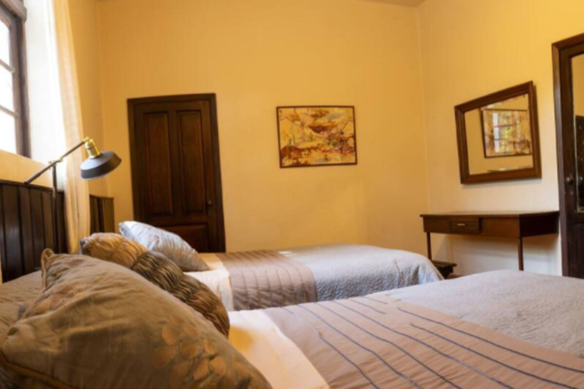 Un dormitorio con dos camas, un escritorio, una silla, una lámpara y un espejo.